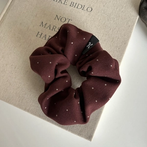 Polka dot oversized scrunchie in burgundy red fabric with a bow logo on a book