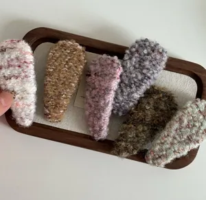 Detailed view of six fuzzy plush hair clips in assorted warm colors on a wooden tray