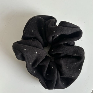Detail view of the soft chiffon fabric with white polka dots on this black scrunchie accessory