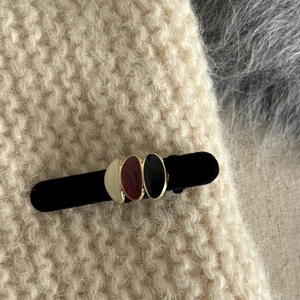 Close-up of black velvet hair clip with three colorful enamel ovals on knit background