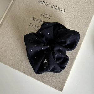 Close-up of a navy blue polka dot scrunchie with a bow tag on a beige cloth book