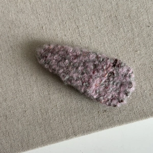 Detail of a mauve plush knit teardrop BB hair clip on a textured linen background