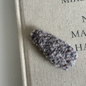 Close-up of a grey plush tweed hair clip on a minimalist fabric book background
