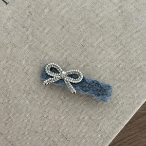 Knitted denim blue hair clip with pearl and rhinestone bow on beige fabric