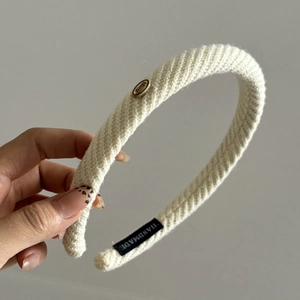 Detail of cream white knitted headband with golden Wings metal tag and handmade label