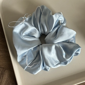 Detailed view of light blue satin scrunchie with white pearls and silver ribbon bow