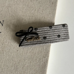 Détail d'une pince à cheveux en velours côtelé gris à pois et lettrage Goodluck doré