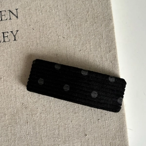 Gros plan sur la barrette en velours noir à pois posée sur une toile beige texturée
