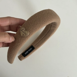 Detail eines handgefertigten gepolsterten Woll-Stirnbandes in Khaki mit Herzanhänger