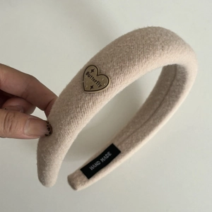 Detail eines beige Fleece-Haarreifs mit Herz-Metallanhänger und handgefertigtem Etikett