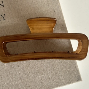 Detail of large rectangular claw clip with amber wood grain texture on beige linen cloth