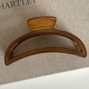 Detail view of large semicircular wood grain hair claw clip for elegant bun hairstyles