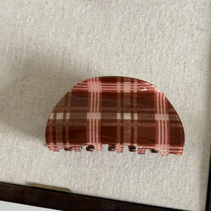 Detailed close-up of retro red-brown plaid hair claw clip on linen background