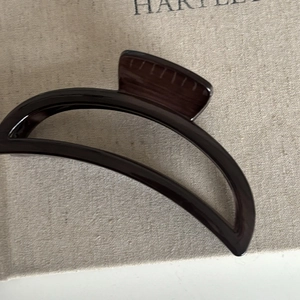 Macro view of a dark brown crescent-shaped hair claw clip with a glossy wood-like finish