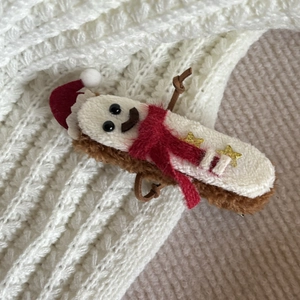 Close-up of plush Gingerbread Man hair clip with red Santa hat on white knit background