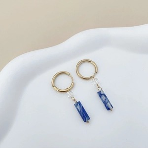 Detail of gold hoop earrings with blue marble resin and clear cube charms on white plate