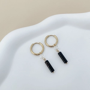Detail of gold hoop earrings with clear faceted beads and black marble cylinders on tray