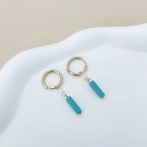 Close-up of gold geometric earrings with clear beads and turquoise stone cylinders