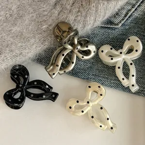 Polka dot bow hair clips in black, grey, beige and cream colors displayed on fabric background