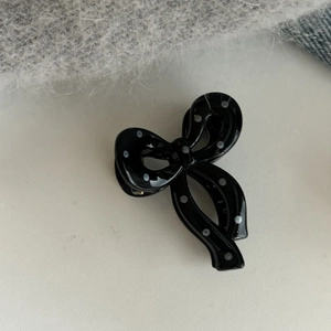 Detailed view of small black acrylic hair claw with white polka dots and ribbon bow