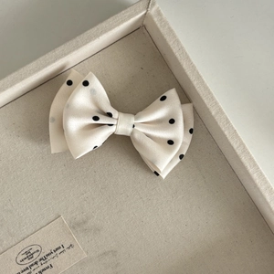 Elegant cream bow hair claw clip with black polka dots shown on a fabric tray