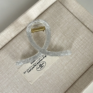 Detail of glitter silver hair claw clip with gold spring on beige textured background