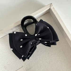 Detailed view of black and white polka dot bow hair claw clip on a fabric tray