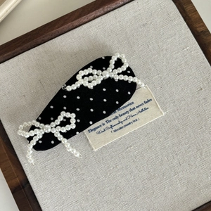 Détail d'une pince à cheveux noire à pois avec deux nœuds élégants en perles blanches sur tissu