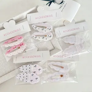 Dettaglio di fermagli per capelli a nuvola con pois e fiocchi nella loro confezione