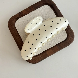 Détail de la pince à cheveux blanc nacré à pois noirs sur un plateau en bois