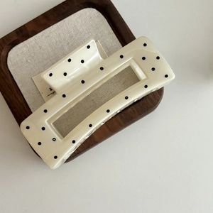 Détail d'une élégante pince à cheveux crème à pois noirs sur un plateau en bois chic