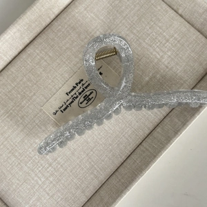 Macro shot of a sparkling silver hair claw clip with glitter finish on a beige tray