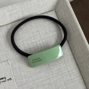 Detailed macro view of black elastic hair tie with green France Handmade resin accent