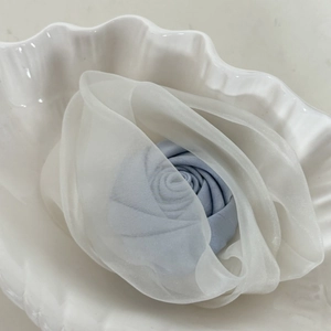 Detail of a handmade white organza rose clip with a blue center in a shell dish