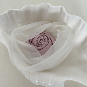 Detail of a handmade pink fabric rose hair clip with white organza petals in a shell tray