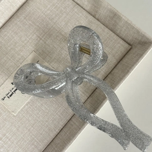 Elegant silver glitter hair claw clip with bow design on a minimalist gift box