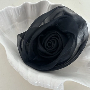 Detail of multi-layered black mesh rose hair clip on white seashell ceramic plate