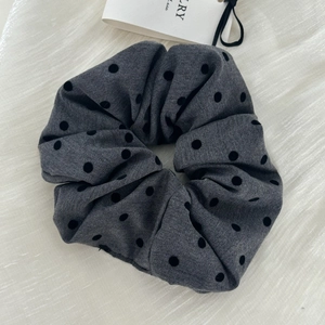 Detailed view of large grey scrunchie with black polka dots on soft satin fabric background