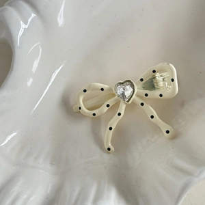 Detail of a creamy white hair clip with black polka dots and a heart crystal centerpiece