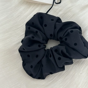 Detailed macro view of black satin polka dot scrunchie with soft velvet flocking texture