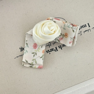 Gros plan d'un chouchou floral avec une grande rose en satin crème et bordure dentelle