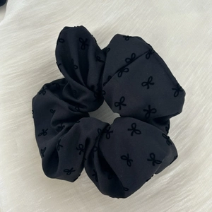 Detail of black satin scrunchie featuring textured flocking bow patterns and soft fabric