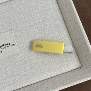 Detail of yellow acetate hair clip with France Handmade text on beige linen tray