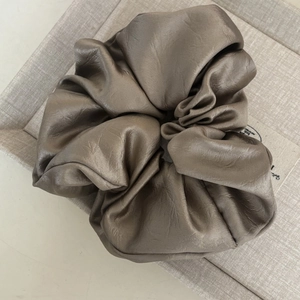 Chouchou en satin bronze élégant avec texture plissée sur plateau en lin beige clair