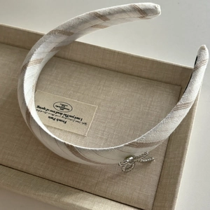 Détail du serre-tête large en tissu à rayures beige avec nœud décoratif en métal argenté