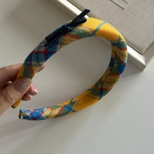 Yellow plaid headband with a denim bow accessory held by hand against a white table