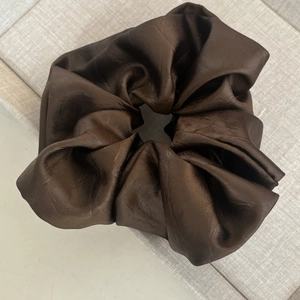 Gros plan d'un grand chouchou en satin marron foncé montrant la texture lisse et les plis doux