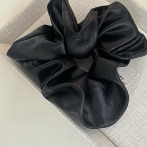 Détail d'un chouchou en similicuir noir montrant sa texture riche et son volume plissé