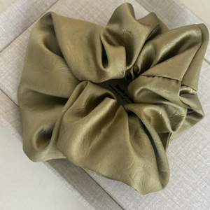 Gros plan d'un grand chouchou en satin vert olive avec texture en soie lisse et plis