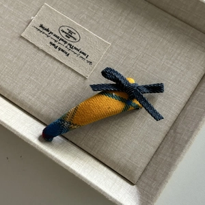 Detail of carrot-shaped plaid fabric hair clip with a blue denim bow in a gift box
